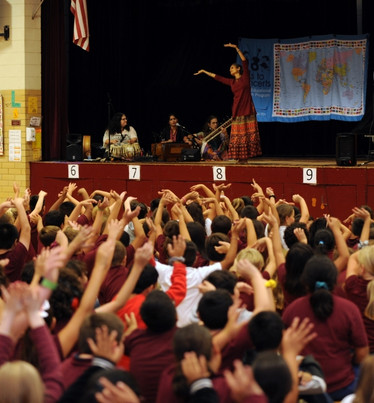 School Concerts_MBAW Programs Photo_Mobile Schoolkids raising their hands with Indian artists onstage.