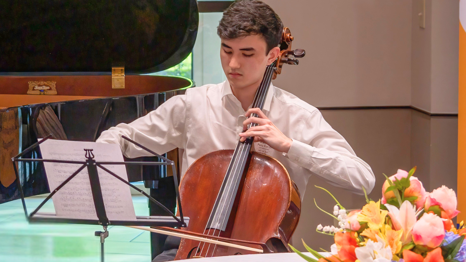 Young female violinist with curly blonde hair in a pink top playing violin with eyes closed in front of a grand piano and garden window